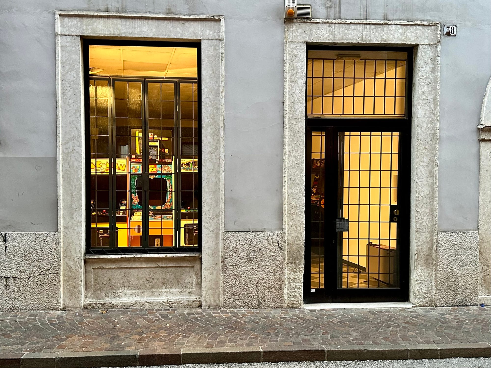 Image of the fron t of a store with a big window and a door with yellow glow lighting inside and video games behind a gate